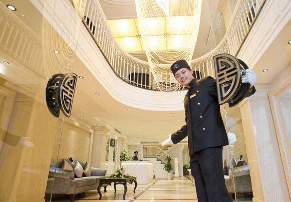 A grand lobby with a curved staircase, a reception desk, and a plush sofa.