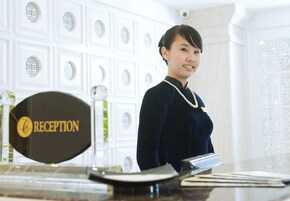 A reception desk with a sign labeled "RECEPTION" and a woman standing behind it.