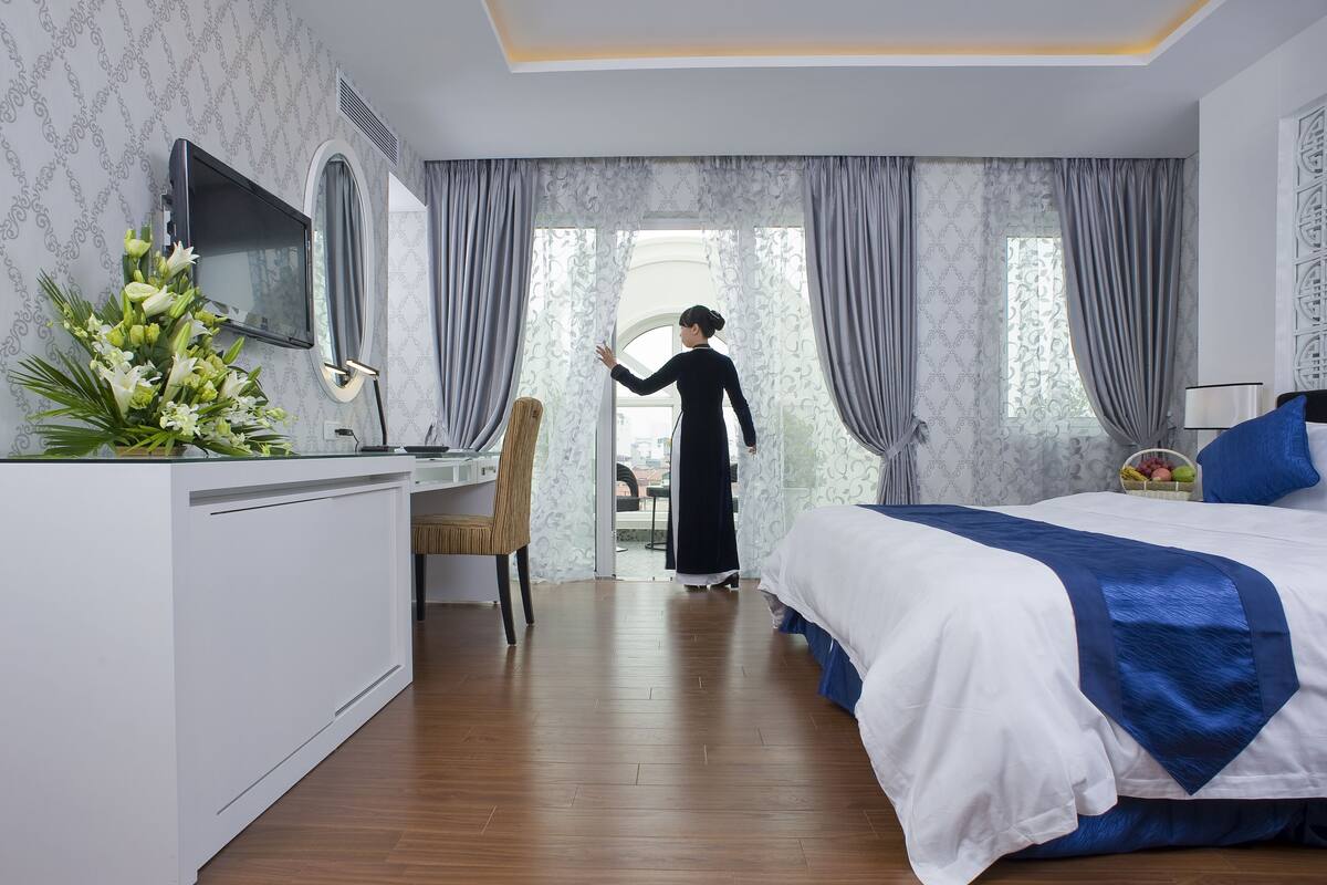 A hotel room with a bed, desk, chair, and a TV on the wall.