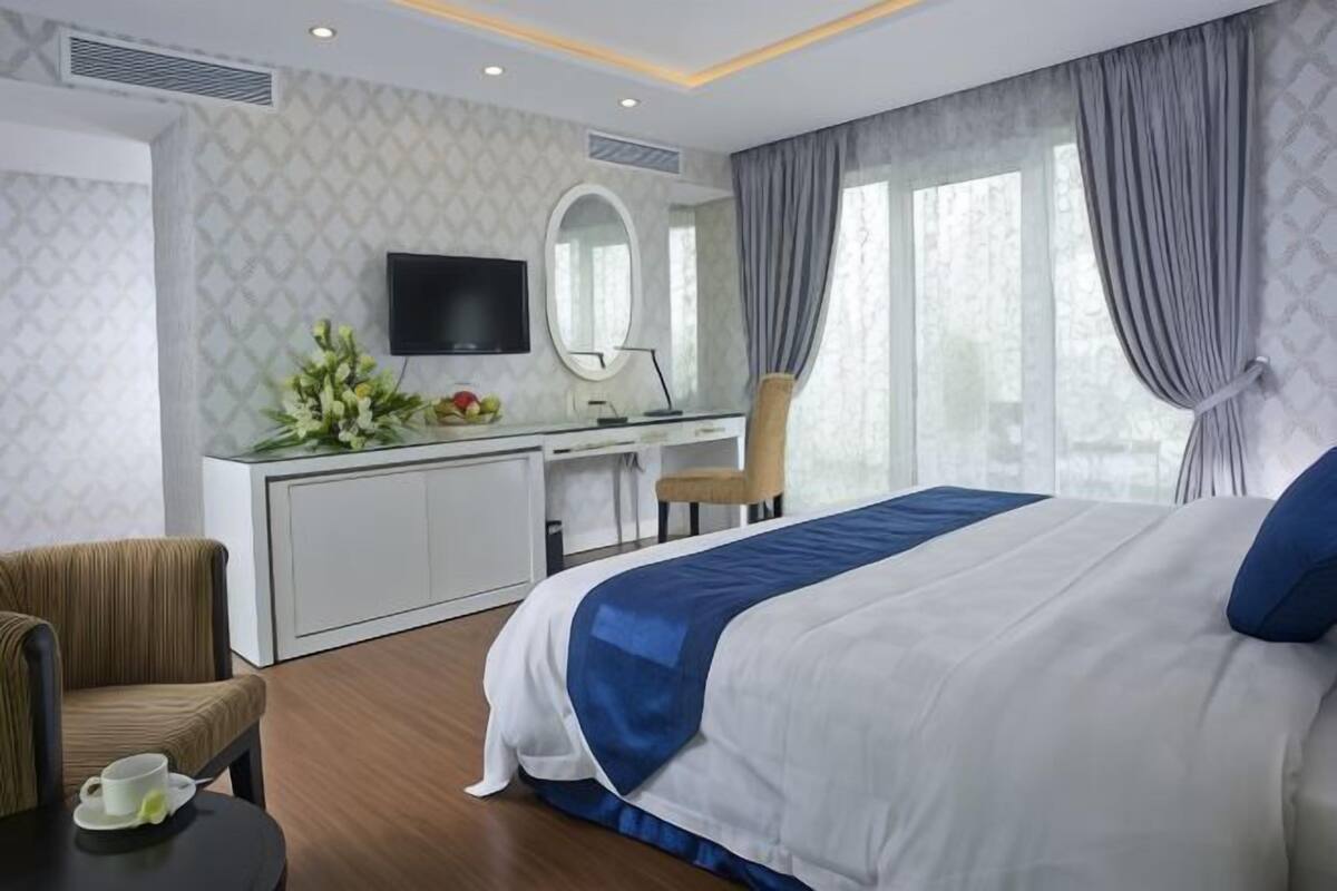 A hotel room with a bed, a desk, a chair, a television, and a window with curtains.