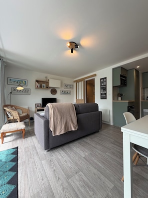 En moderne stue med en grå sofa, en træstol, et spisebord og et køkkenområde.