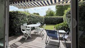 Eine Terrasse im Freien mit Tisch, Stühlen, einem Grill und einem überdachten Bereich mit Streifenmarkisen.