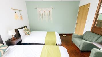 Une chambre d’hôtel avec deux lits, un fauteuil vert, une table de chevet en bois avec une lampe et une décoration murale.