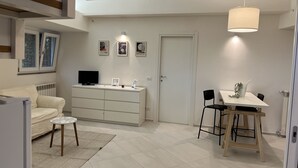 Uma sala de estar moderna com sofá, televisão, mesa de jantar com cadeiras e luminária pendente.