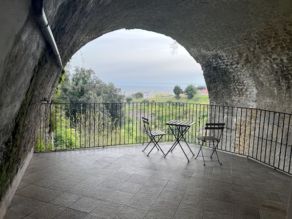 A balcony with a stone arch, a table, two chairs, and a view of the sea and greenery. - Maison exclusive posillipo M&J (Napoli)