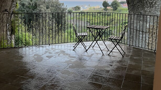 Um alpendre coberto com vista para o mar, com uma mesa e cadeiras.