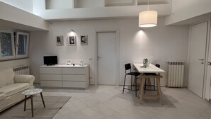 Uma sala de estar moderna com sofá, mesa de centro, mesa de jantar com cadeiras, televisão e obras de arte na parede.