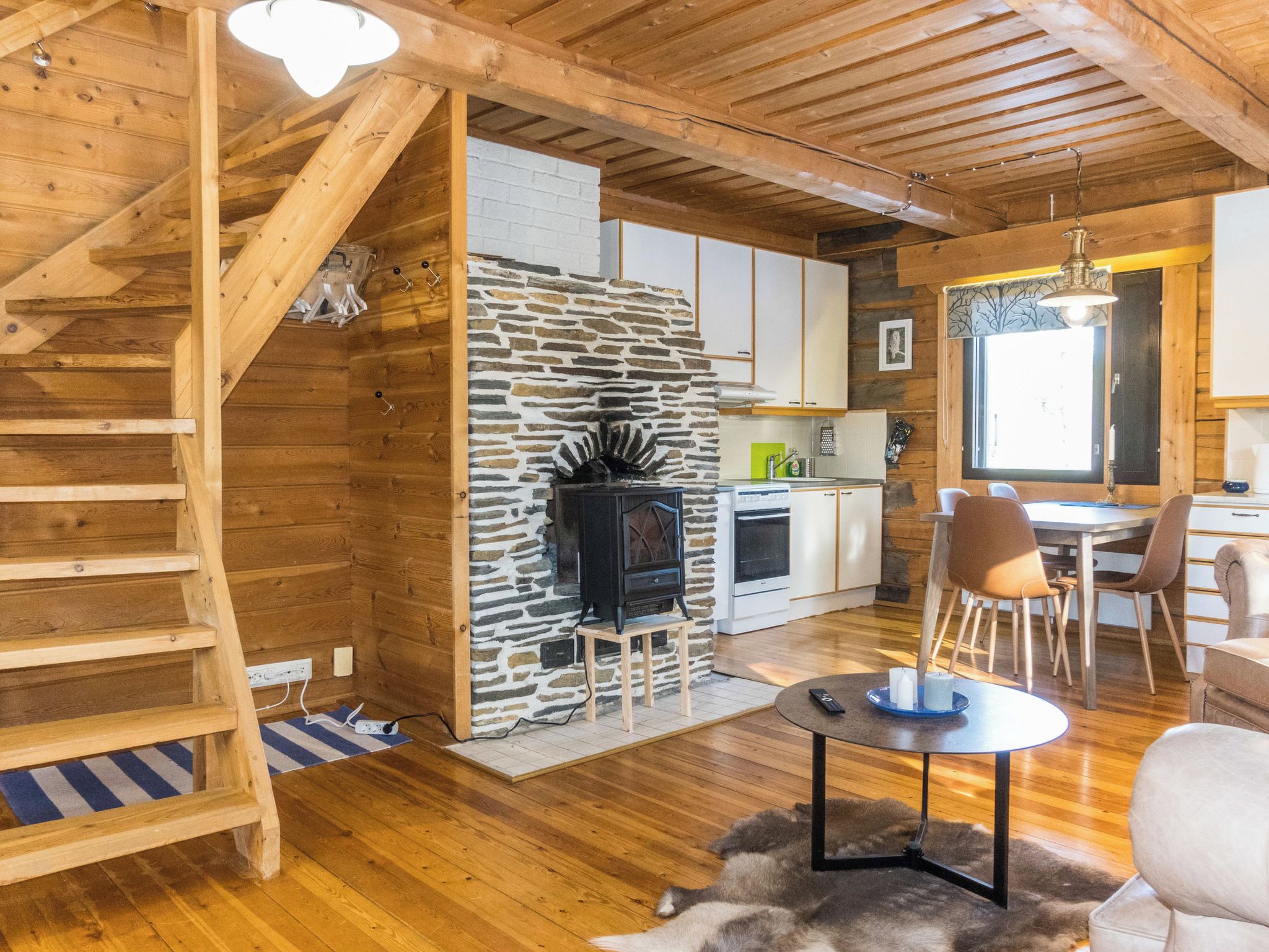 Un intérieur en bois avec une cheminée en pierre, une cuisine et un coin repas comprenant des chaises et une table.