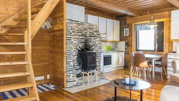 Un interior de madera con chimenea de piedra, una cocina y un comedor con sillas y una mesa.