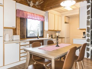 A cozy kitchen with wooden cabinets, a dining table with chairs, and a window with a checkered curtain.
