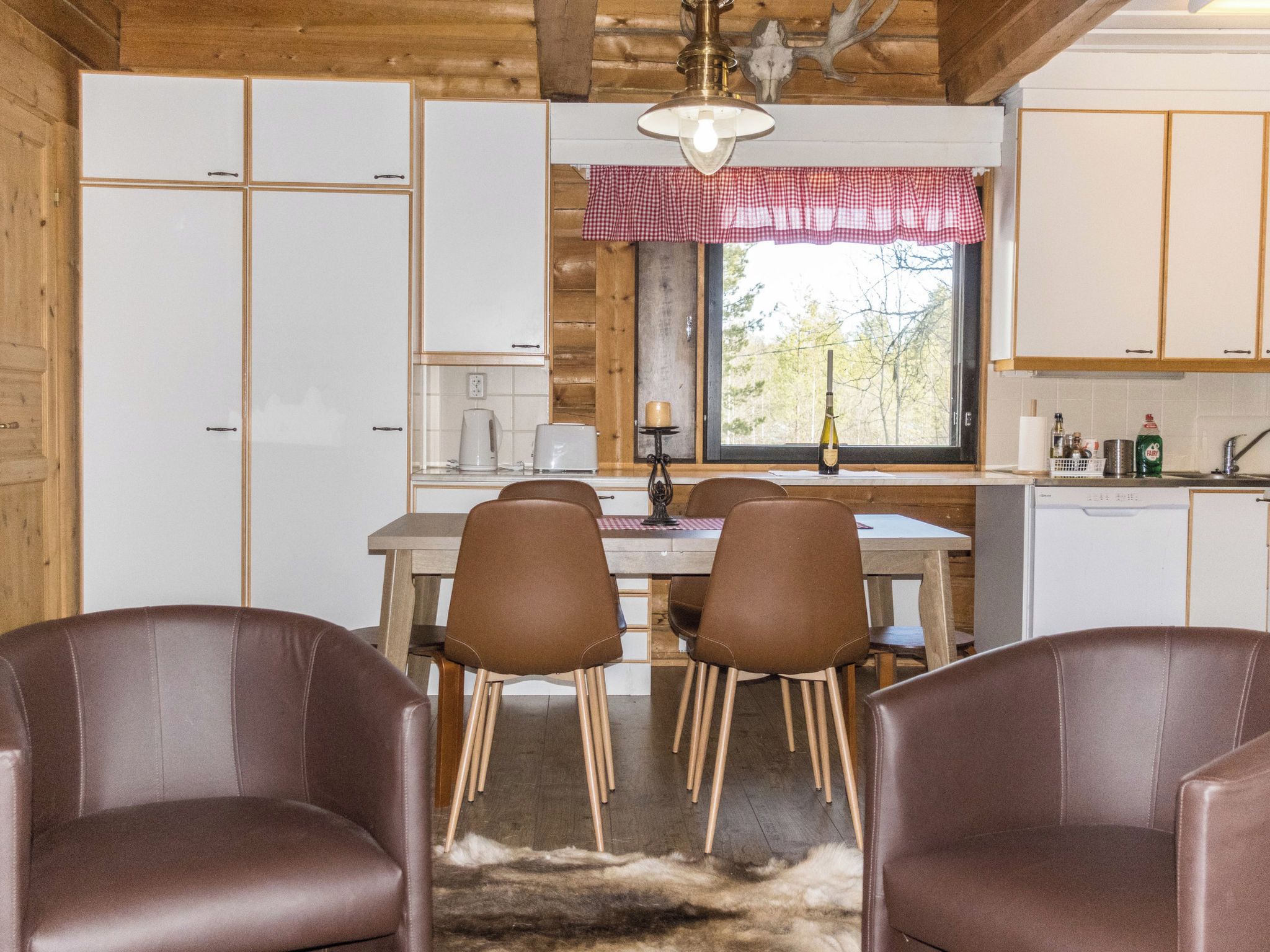 Une cuisine chaleureuse, aménagée dans le style d’un chalet, avec des meubles en bois, une table à manger entourée de chaises et une fenêtre donnant sur la forêt.