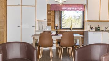 Een gezellig keuken in blokhutstijl met houten kastjes, een eettafel met stoelen en een raam met uitzicht op bomen.