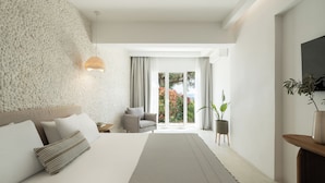 A modern hotel room with a large bed, a textured wall, a view of the outdoors, and a small seating area. - Oniro Skiathos (Skiathos)