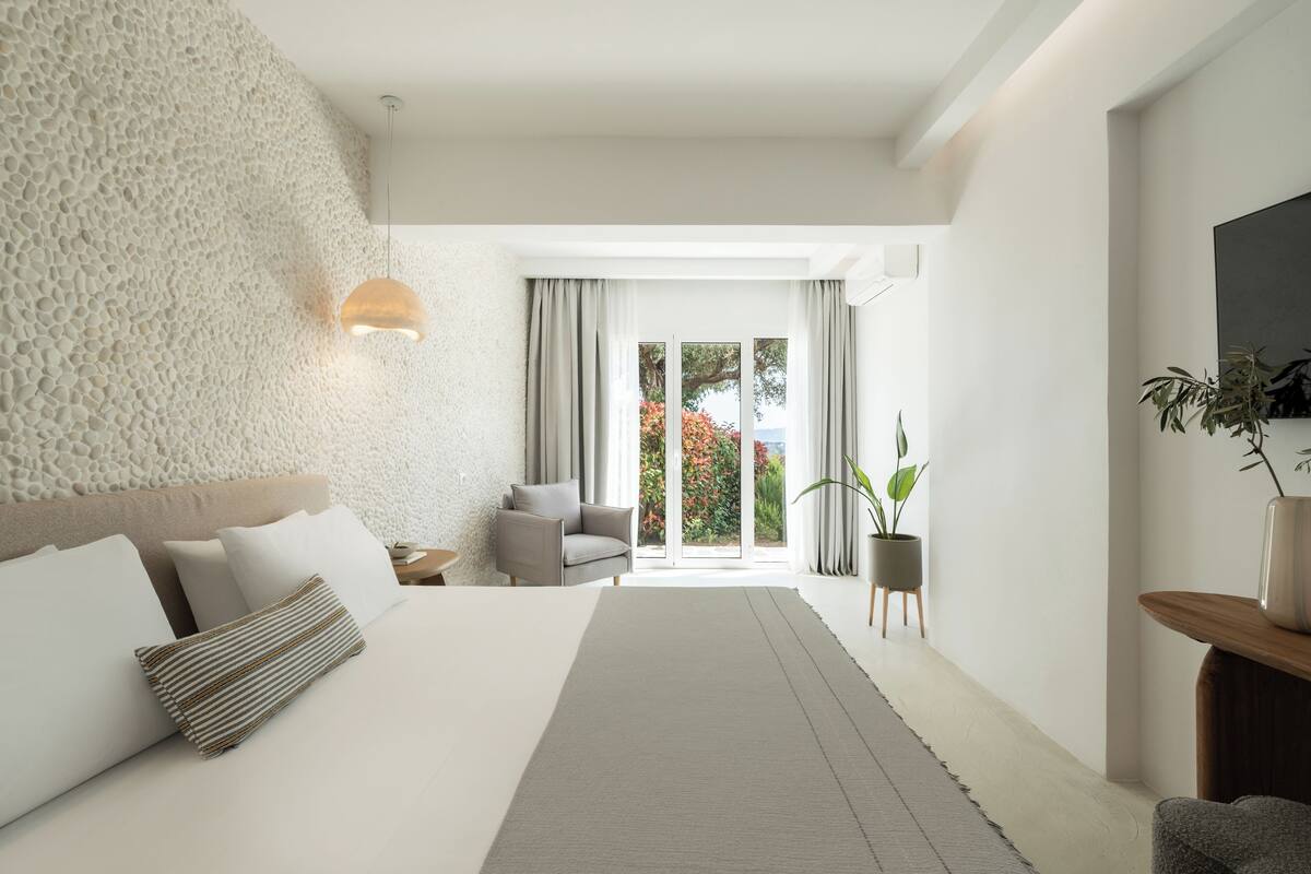 Una habitación de hotel moderna con una cama grande, una pared con textura, vistas al exterior y una pequeña zona de estar.
