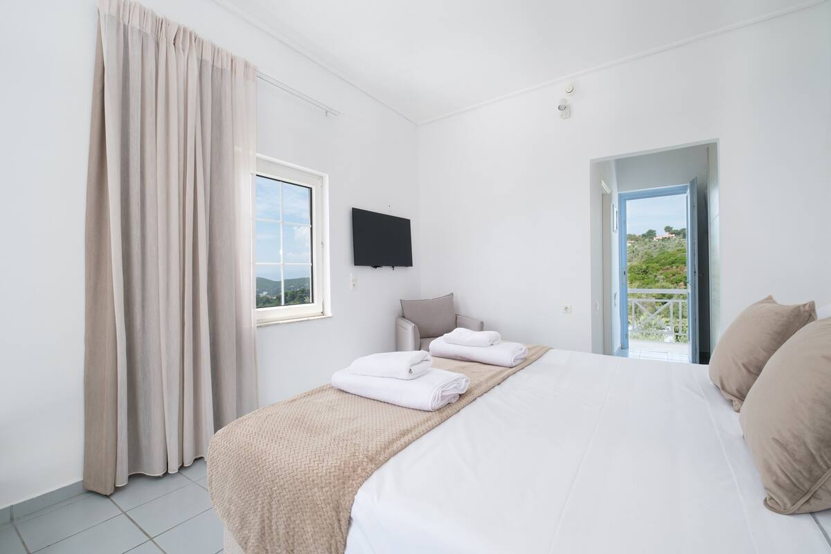 Un dormitorio con cama, televisión, ventana y puerta que da a un balcón.