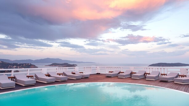 A poolside area with lounge chairs and a view of the sea and mountains. - Oniro Skiathos (Skiathos)