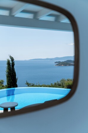 A view through a window of a pool with a clear blue sky and distant land. - Oniro Skiathos (Skiathos)