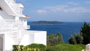 A white building with a balcony overlooking a clear blue sea and a distant island. - Oniro Skiathos (Skiathos)