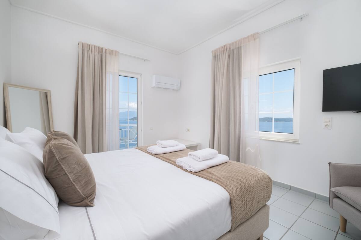 Una habitación de hotel con una cama, dos ventanas, un televisor y una silla.