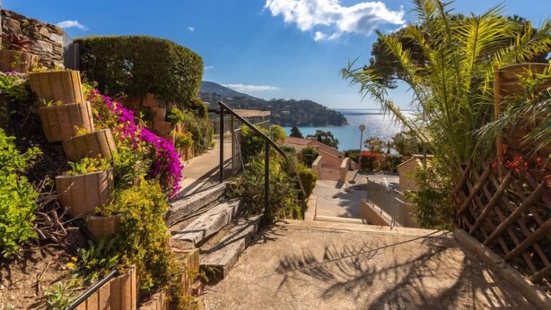 Un sentiero costiero con gradini che portano a una vista panoramica del mare e un'isola in lontananza.