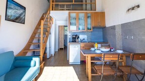 Una cucina compatta con mobili in legno, una zona pranzo con tavolo e sedie, una scala e un divano blu.