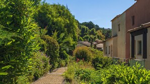 Ein Weg, der durch einen Garten mit dichtem Grün und ein Gebäude mit einem Ziegeldach führt.