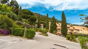 Une rue résidentielle bordée de maisons, avec un ciel dégagé et une végétation variée comprenant des arbres et des arbustes.