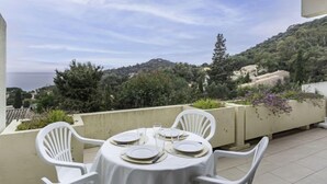 Une table ronde entourée de chaises blanches, placée sur une terrasse et offrant une vue panoramique sur des collines et un plan d’eau.