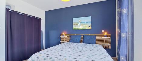 A bedroom with a bed, a painting, a bedside table, and a hanging light fixture.