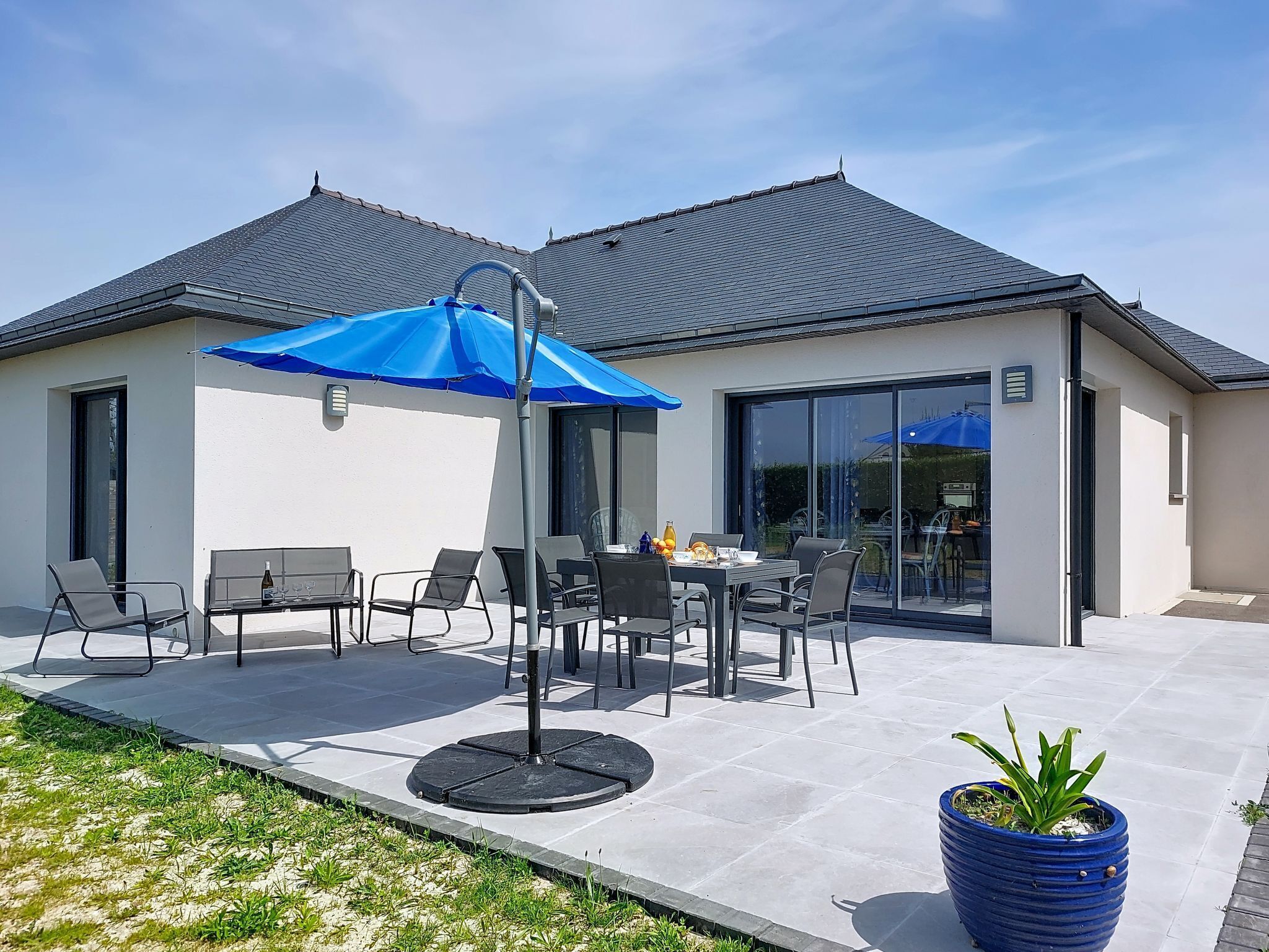 A modern house with a patio, outdoor seating, and a large blue umbrella.