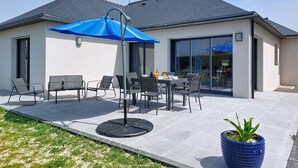 Une maison moderne dotée d’un patio, d’un espace salon extérieur et d’un grand parasol bleu.