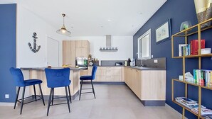 Une cuisine moderne dotée d’un îlot central, de tabourets de bar et d’une bibliothèque remplie de livres.