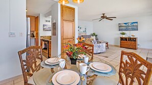 A dining area with a table set for four, a ceiling fan, and a kitchen in the background.