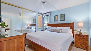A hotel room with a large bed, a wooden dresser, a bedside table with a lamp, and a mirror.