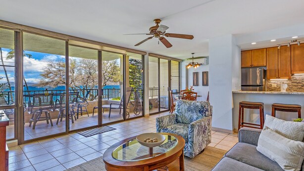 A spacious living area with a large sliding glass door leading to a balcony with outdoor seating and a view of the ocean.