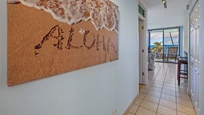 A corridor with a corkboard displaying the word "ALOHA" and a view of a balcony with outdoor furniture.