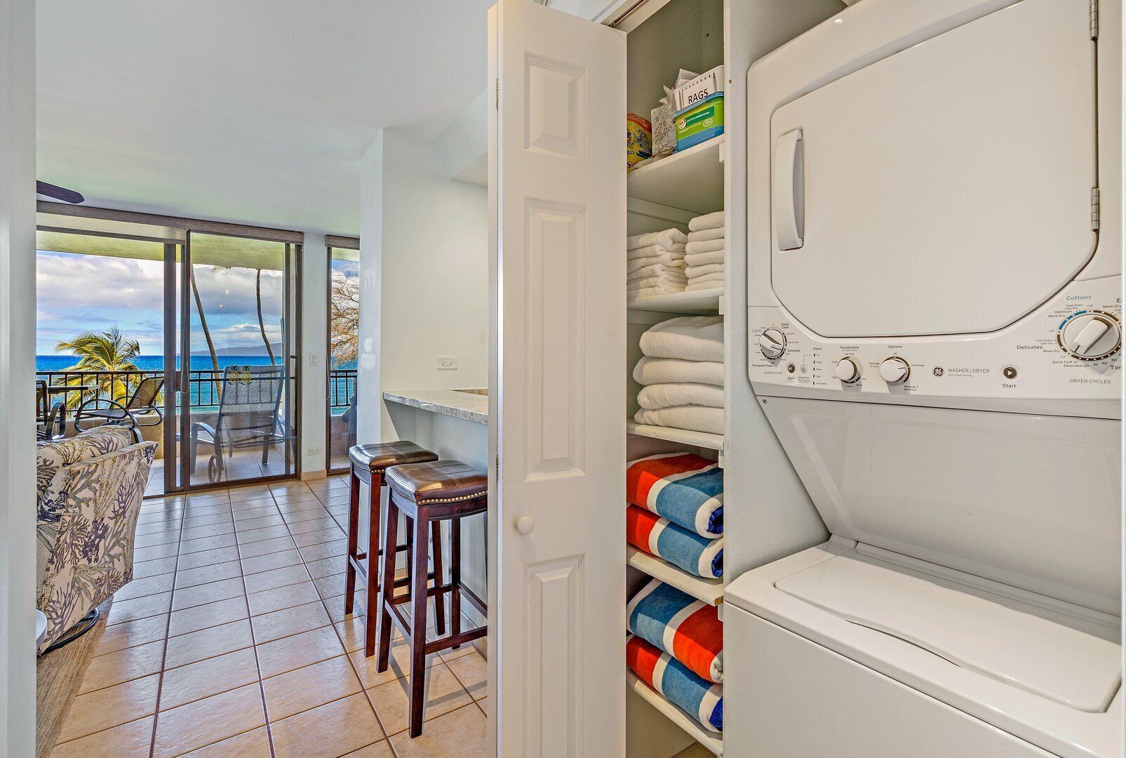 A laundry room with a view of the ocean, a bar area with stools, and neatly folded towels on shelves.