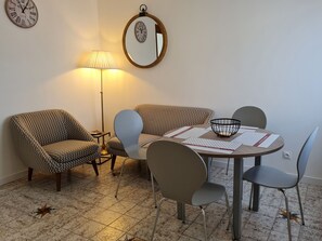 A dining area with a round table, two patterned armchairs, a floor lamp, and a mirror on the wall. - Charming Renovated House with Private Parking, Garden, and Easy Access to Nancy (Lunéville)