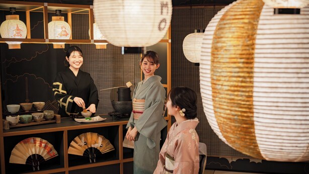 Un ambiente tradicional japonés con una ceremonia del té, incluyendo un hervidor, tazas y abanicos.