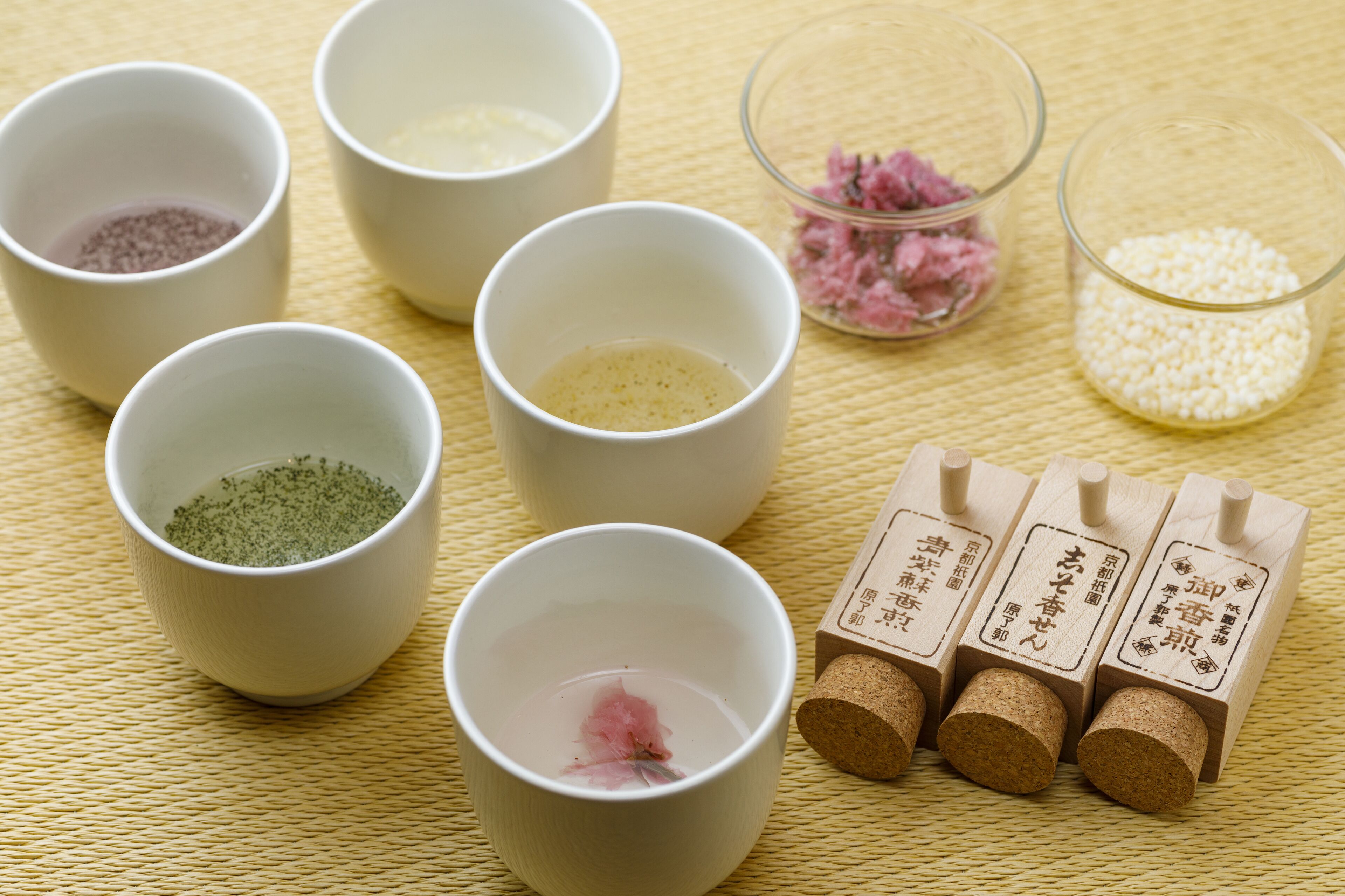 Six white cups with different colored powders, a small bowl of pink powder, and four wooden blocks with Japanese characters.