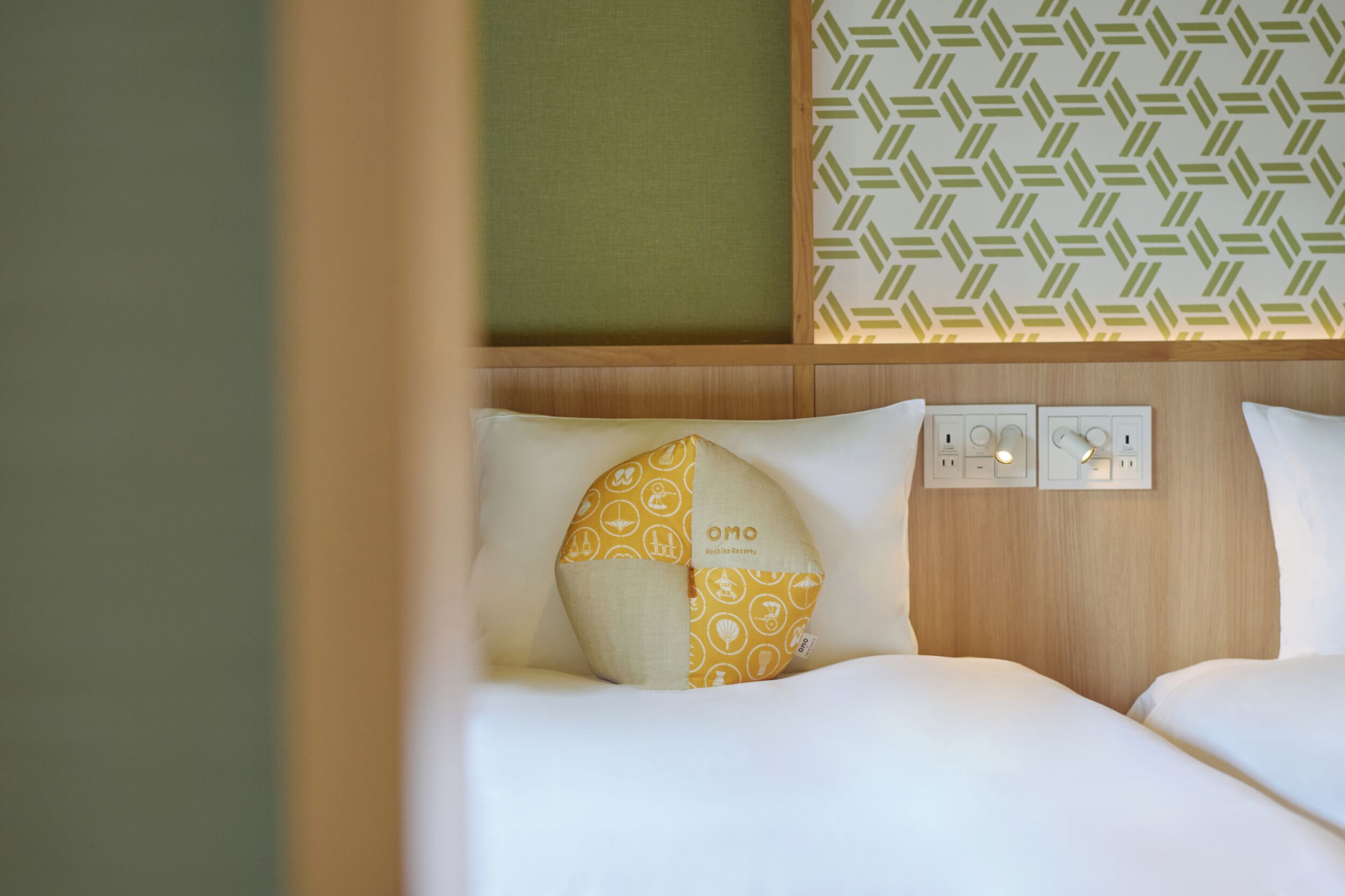 Habitación de hotel con cama, almohada estampada, pared con diseño geométrico y cabecero de madera.