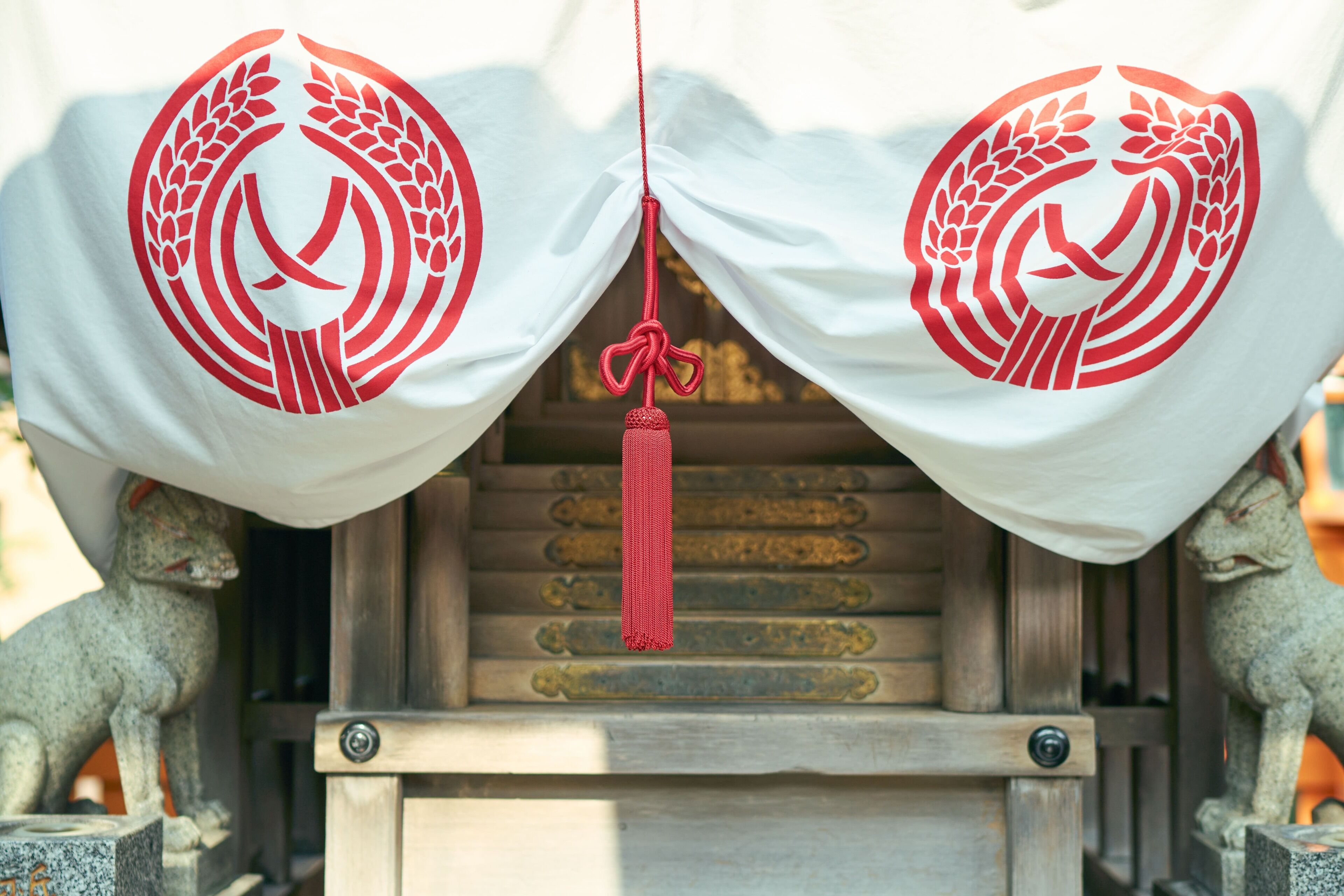A shrine with a white cloth featuring a red emblem, flanked by stone lion statues, and a red tassel hanging from the cloth.