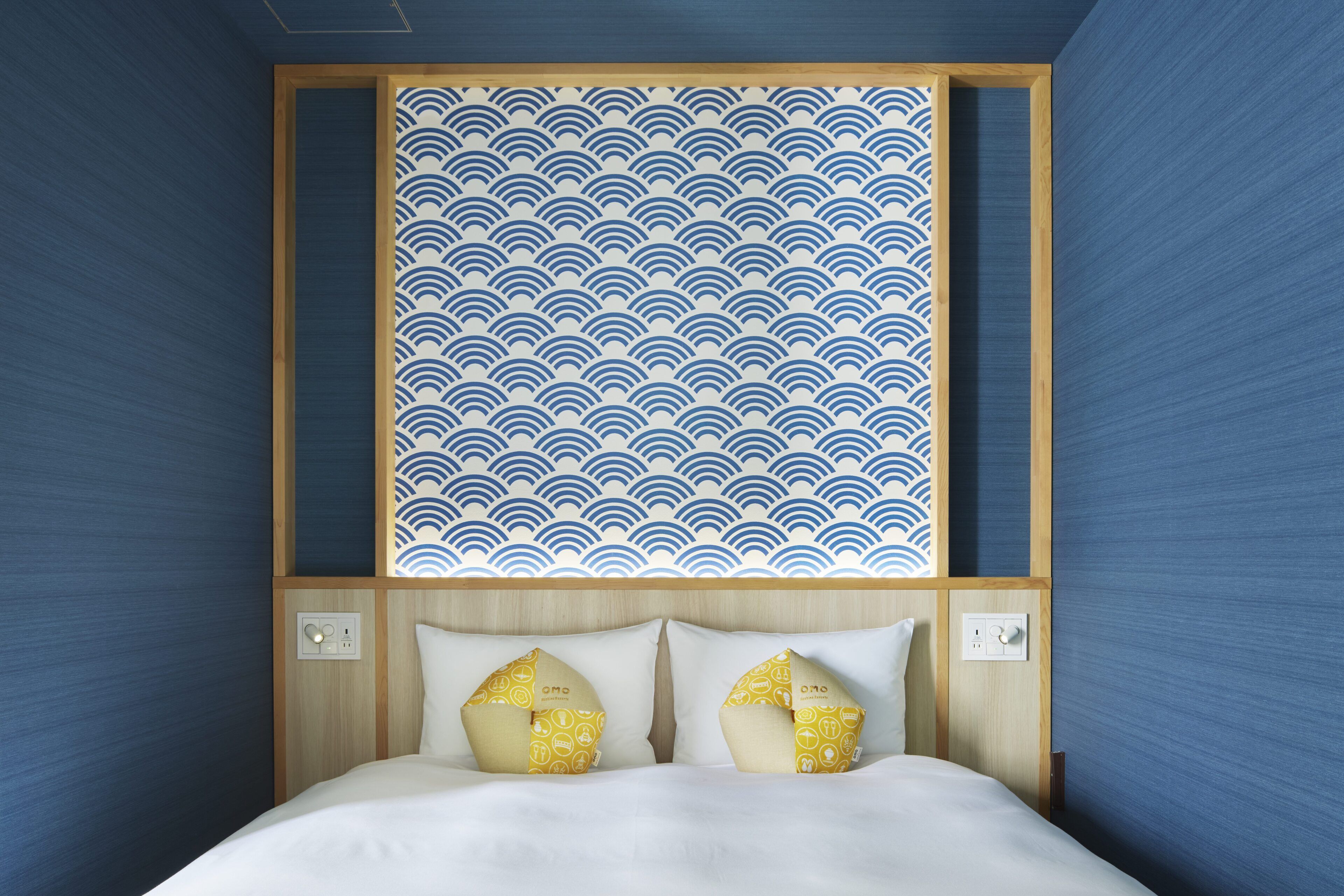 A hotel room with a bed, two pillows, a wall with a wave pattern, and wooden paneling.