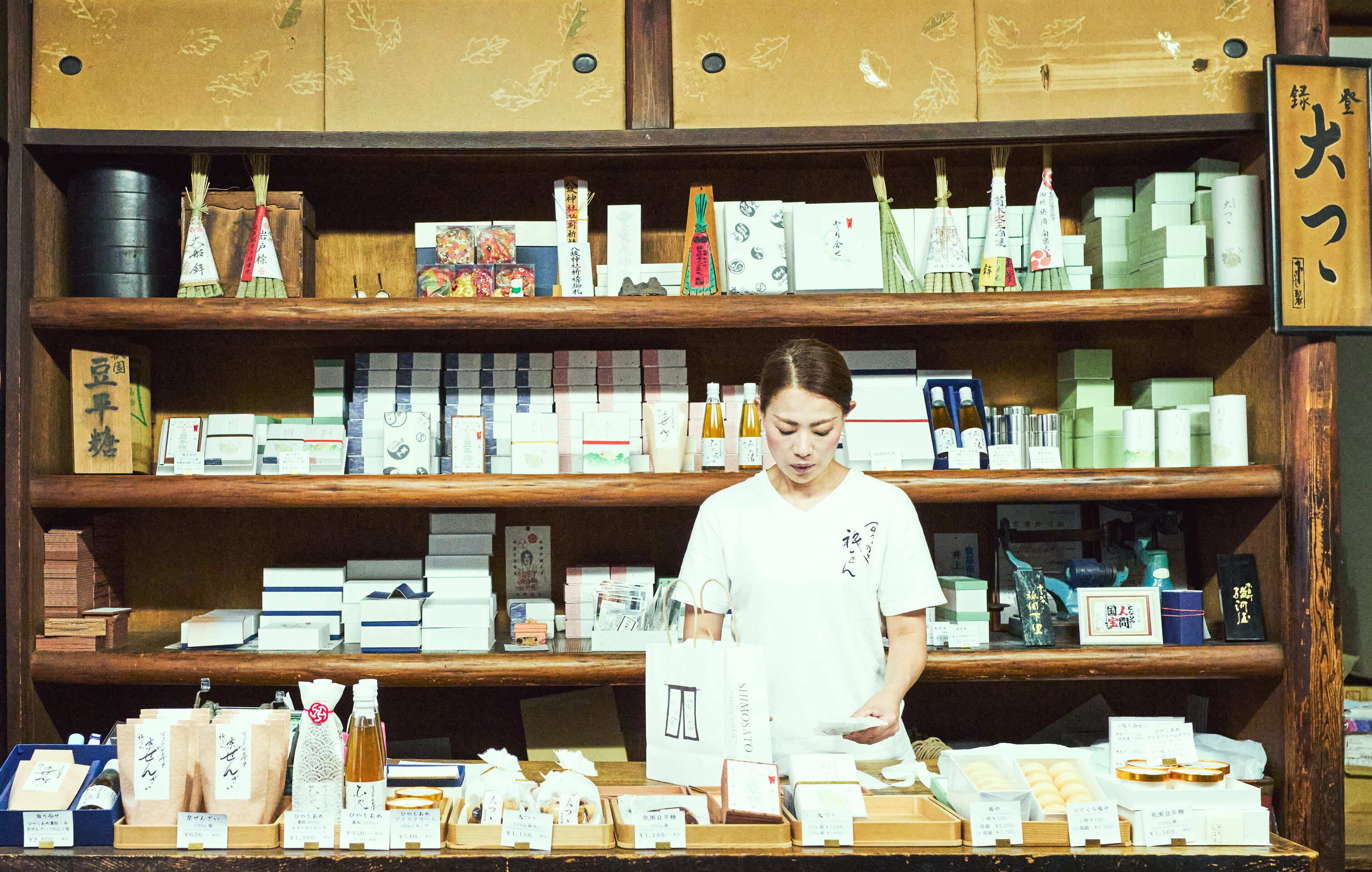 Une personne se tient derrière un présentoir où sont exposés divers produits emballés, probablement dans un magasin ou une boutique.