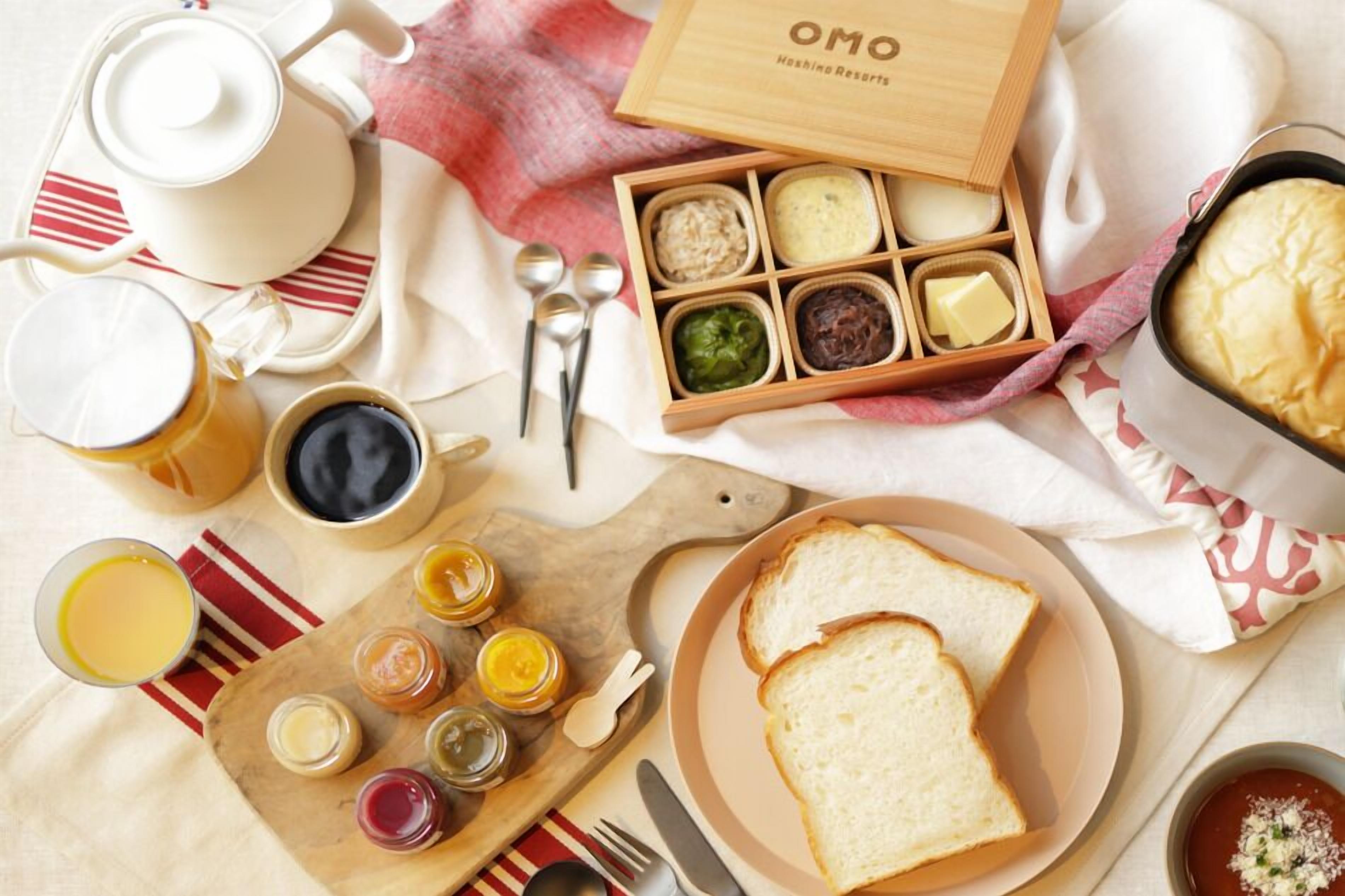 A breakfast setup with a teapot, cups, a wooden box of spreads, a pie, and toast on a table.