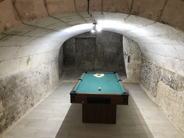 A pool table in a room with stone walls and a vaulted ceiling.