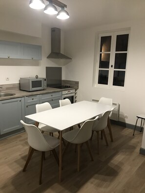 A modern kitchen with a white table and chairs, a microwave, stove, and a window with blinds.