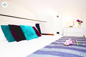A bedroom with a bed, pillows, a bedside table, a lamp, and a vase with flowers.