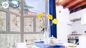 A kitchen with a view of a stone wall, a window with blue curtains, and a table set with tea cups and a teapot.