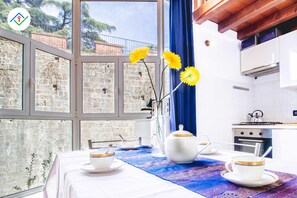 A kitchen with a view of a stone wall, a window with blue curtains, and a table set with tea cups and a teapot.